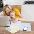 Mother using laptop with baby boy in kitchen at home