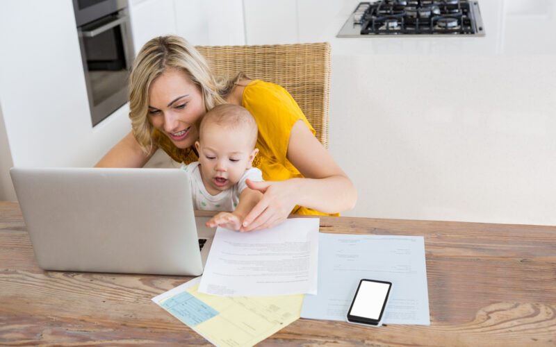 Mother using laptop with baby boy in kitchen at home